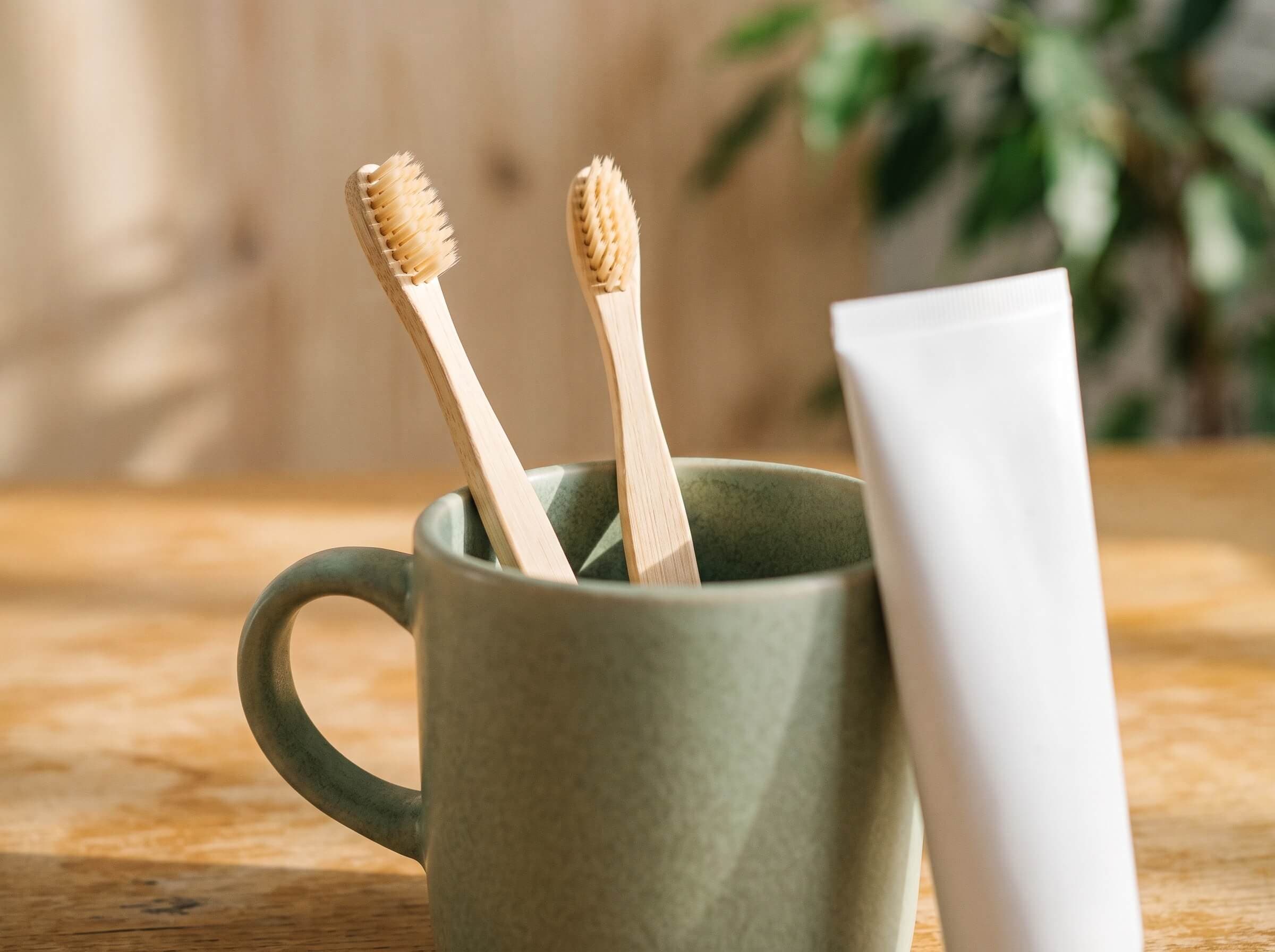 Bambuszahnbürsten im Becher und Zahnpasta auf der Holzablage bei kidsReinisch